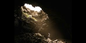 Man in a cave looking up to sunlight coming through a hole in the roof